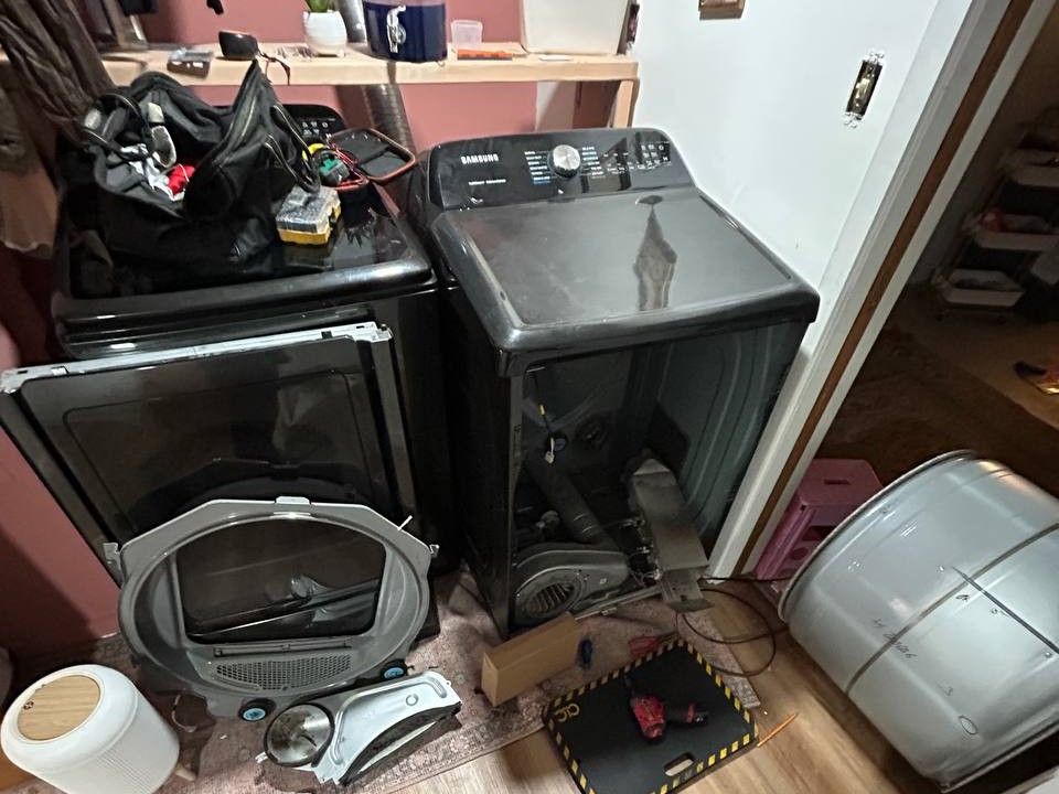 Top-load washer beside a dryer taken apart for repair, drum out on the floor
